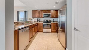 A modern kitchen with wooden cabinets, stainless steel appliances, and a tiled floor. - Southern Comfort at The Aruba (Daytona Beach)