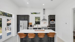 Une cuisine moderne avec un îlot central, des meubles de couleur sombre et une grande fenêtre.