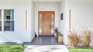Une entrée moderne avec une porte en bois, un banc et un petit espace jardin agrémenté de plantes.