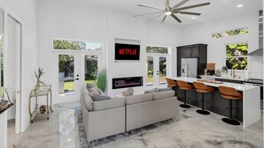 Une cuisine moderne dotée d’un îlot central, de tabourets de bar et d’un téléviseur encastré qui diffuse « NETFLIX ».