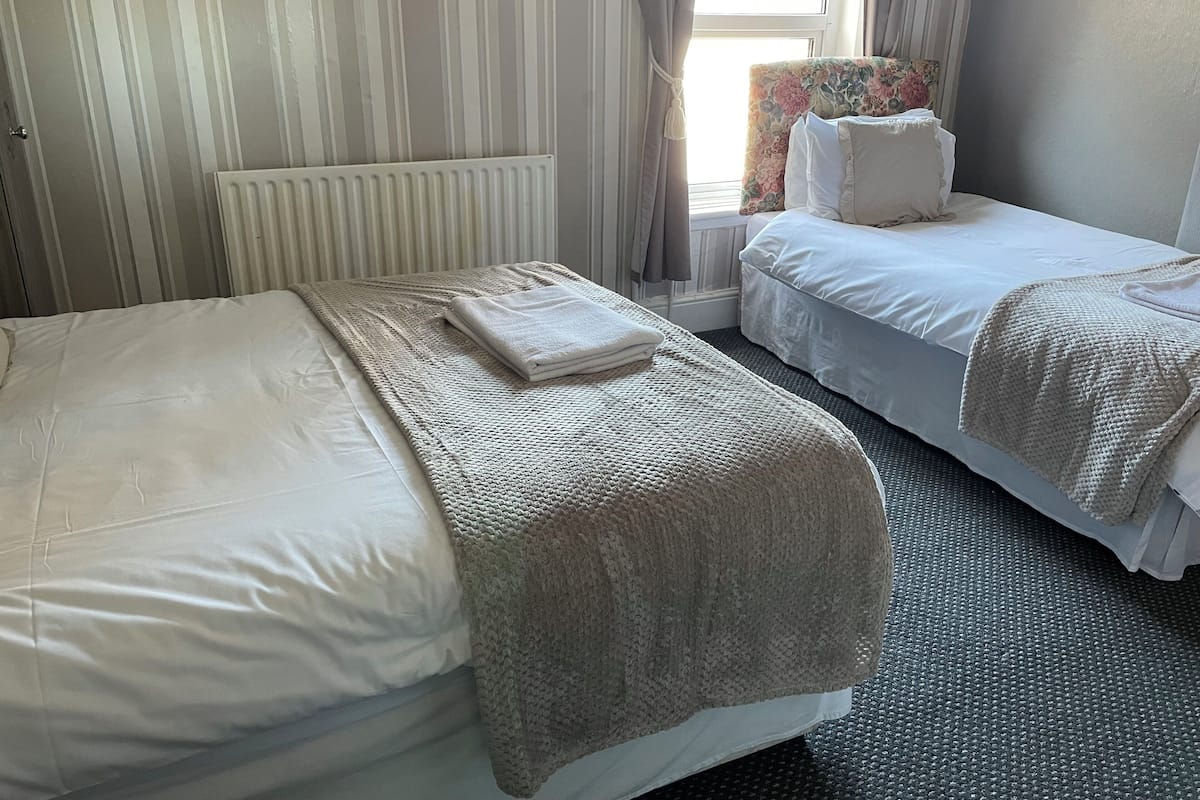 A hotel room with two beds, a radiator, a window with curtains, and a floral chair.
