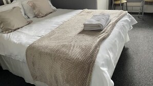 A neatly made bed with a folded towel, a textured throw blanket, and several pillows. - Somerville Hotel (Blackpool)