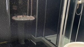 A shower with a glass door, a towel rack, and a toilet in a bathroom with tiled flooring. - Somerville Hotel (Blackpool)