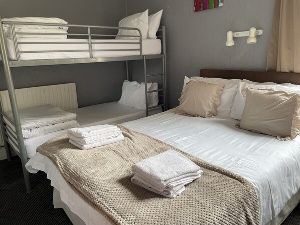 A hotel room with bunk beds, a large bed with white linens, a knitted throw blanket, and a wall-mounted light fixture.