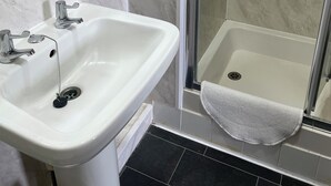 A bathroom with a white sink, a shower with a glass door, and a towel rack. - Somerville Hotel (Blackpool)
