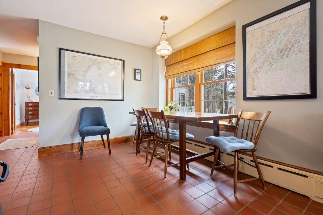 Un coin repas comprenant une table et des chaises, un luminaire suspendu et deux grandes cartes encadrées accrochées aux murs.