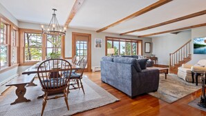 A spacious living room with wooden beams, a dining area with a table and chairs, and large windows offering a view of the outdoors. - Beachfront and Only 30 Steps To Beach! (Saco)