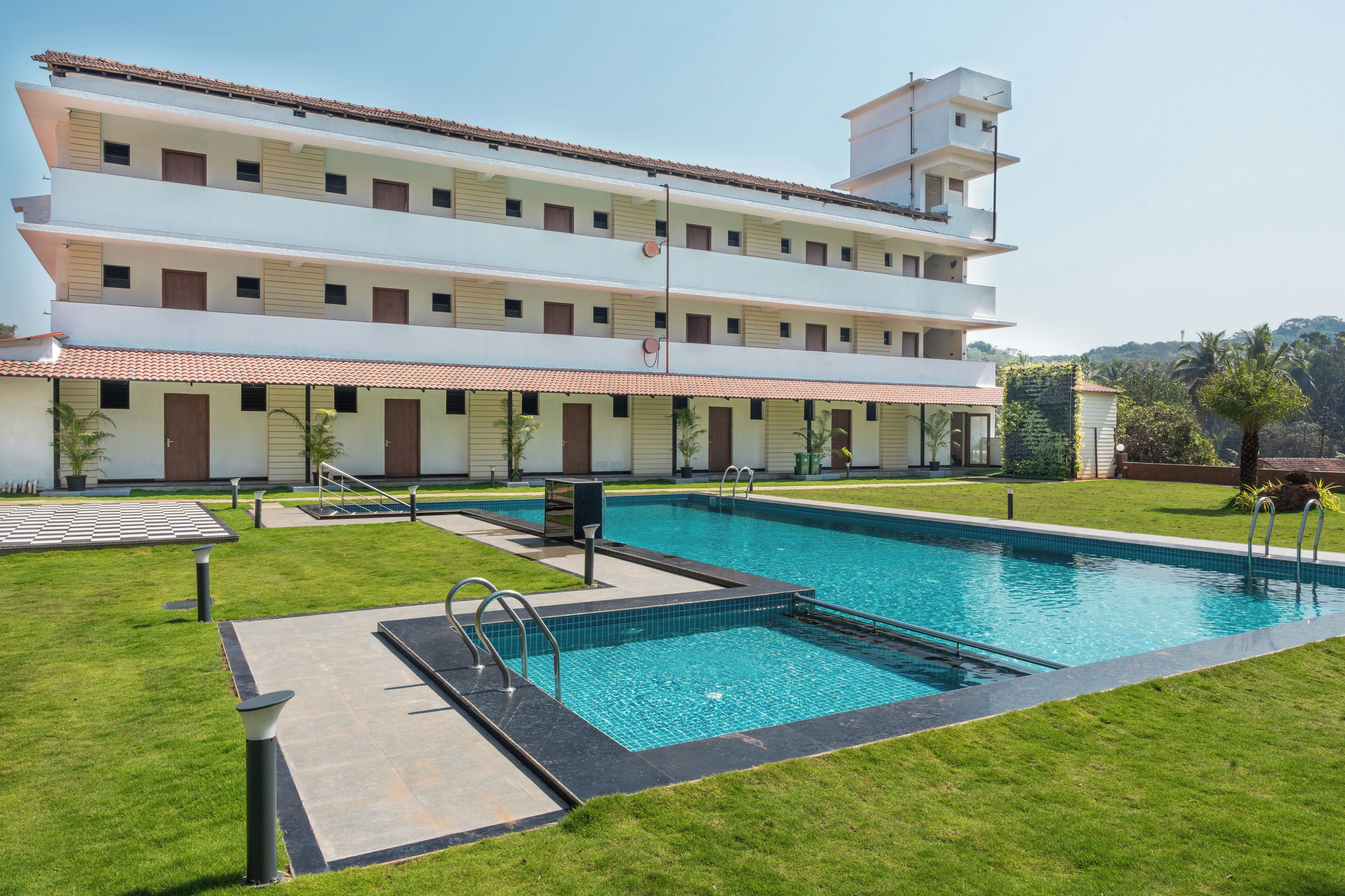 A multi-story hotel with a swimming pool, outdoor seating, and a well-maintained lawn.
