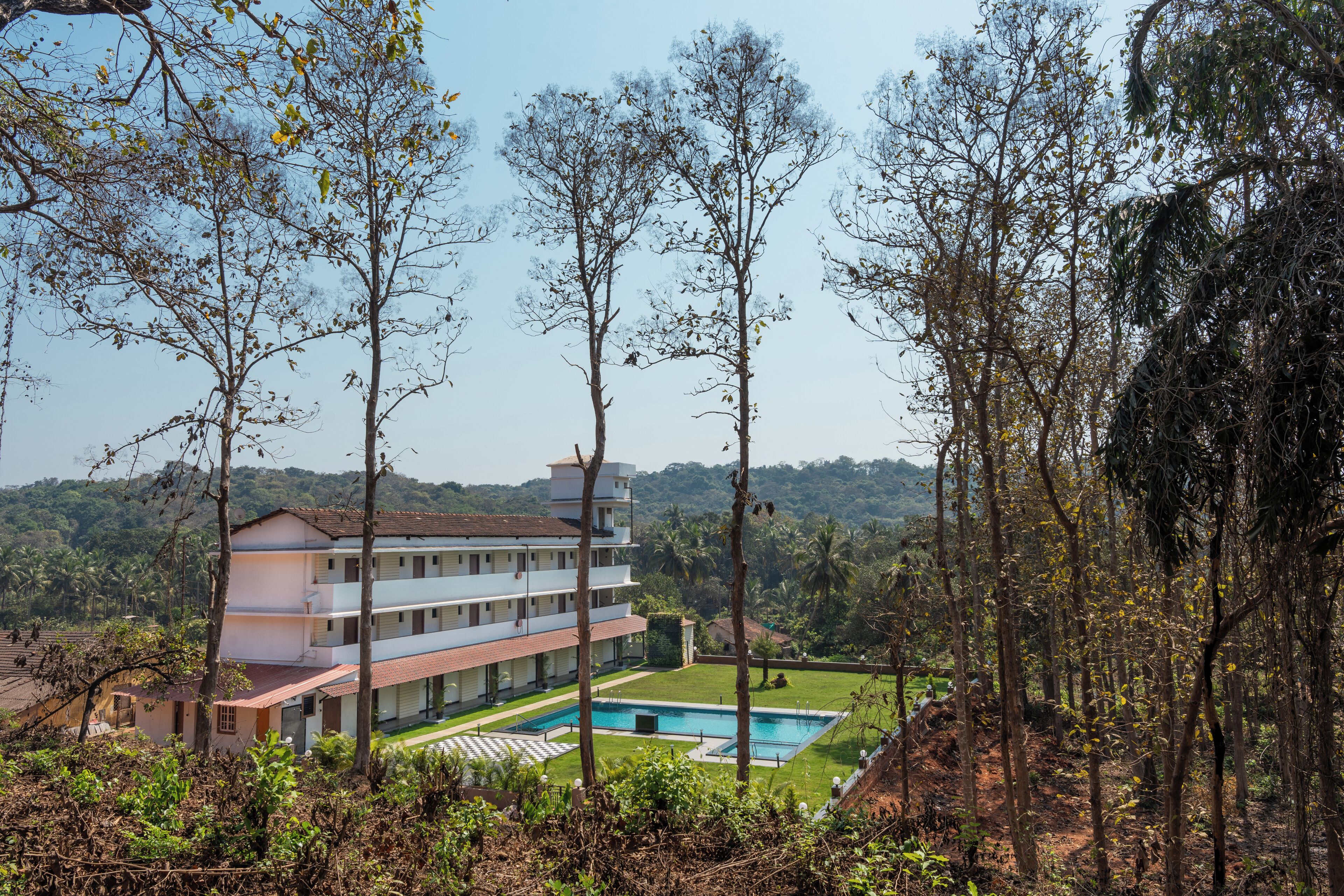 Um hotel de vários andares com piscina, rodeado por árvores e colinas.