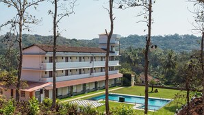 A multi-story hotel with a swimming pool, surrounded by lush greenery and hills. - Hotel Holiday Village (Alto de Porvorim)