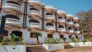 A multi-story building with balconies, a palm tree, and steps leading to the entrance. - Hotel Holiday Village (Alto de Porvorim)