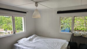 Un dormitorio con cama, dos ventanas, una lámpara colgante y vistas a la vegetación exterior.