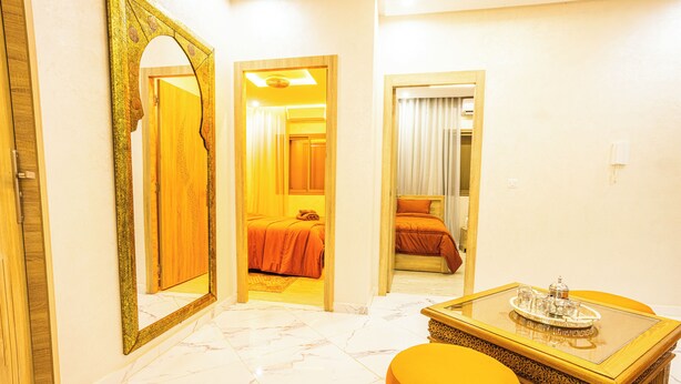 A hotel room with a bed, a sitting area with a table and ottoman, and a mirror with an ornate frame. - Traditional/Modern Apartment, Full A/C, 10m to Airport, 15m to centre. (Marrakech)