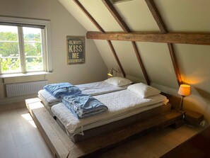 A loft-style bedroom with a sloped ceiling, a bed with two pillows, a bedside lamp, and a window with a view of greenery. - 4 Star Holiday Home in Fagelmara (Fågelmara)