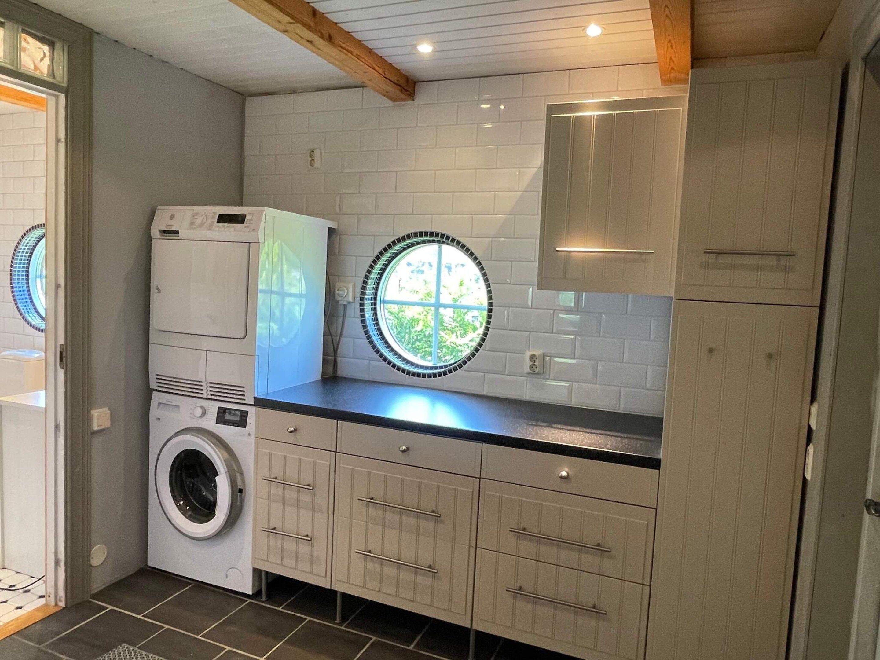 A laundry room with stacked appliances, a window, and cabinets.