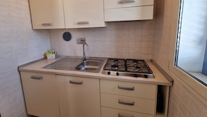 Een kleine keuken met beige kastjes, een roestvrijstalen spoelbak en een gasfornuis.