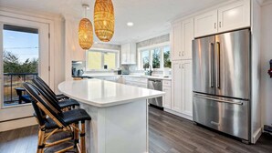 A modern kitchen with white cabinetry, a large stainless steel refrigerator, and a central island with bar stools. - Game Room, Home Gym, 1 Mile to Beach (York Beach)