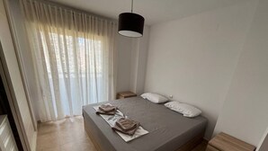 A bedroom with a bed, two bedside tables, a hanging lamp, and a window with sheer curtains.