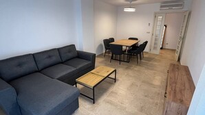 A modern living room with a dark gray sectional sofa, a wooden coffee table, and a dining area with a table and chairs.