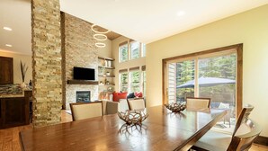 A spacious dining area with a large wooden table, stone accent walls, and a view of the outdoors.