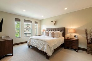 Quarto com cama grande, mesa de cabeceira com abajur, cômoda de madeira e decoração de caveira de boi na parede.