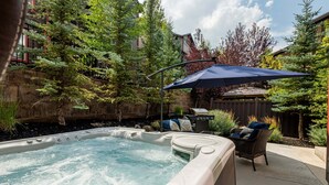 A hot tub with a patio area, surrounded by trees and a wooden fence.