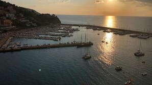 A coastal marina with boats docked, a pier, and buildings on a hillside.