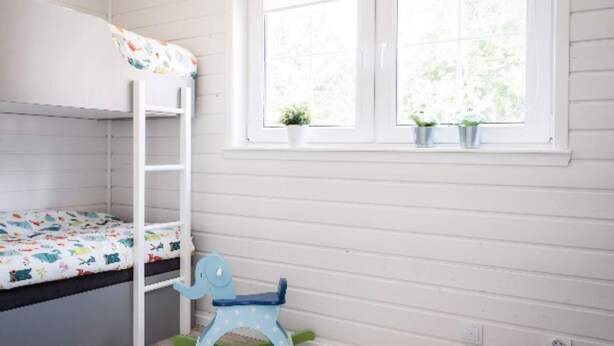 Letto a castello per bambini con copriletto colorato, una poltrona a dondolo e una finestra con due piante in vaso.