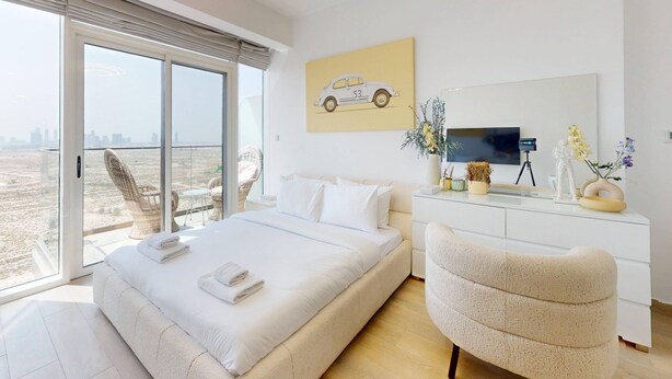 Une chambre d’hôtel moderne dotée d’un grand lit, d’un coin salon, d’un bureau avec une télévision et d’un balcon offrant une vue sur la ville.