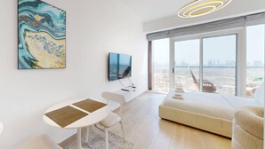 Un salon moderne doté d’une grande fenêtre, d’un téléviseur à écran plat, d’un coin repas avec une table et des chaises, et d’un canapé.