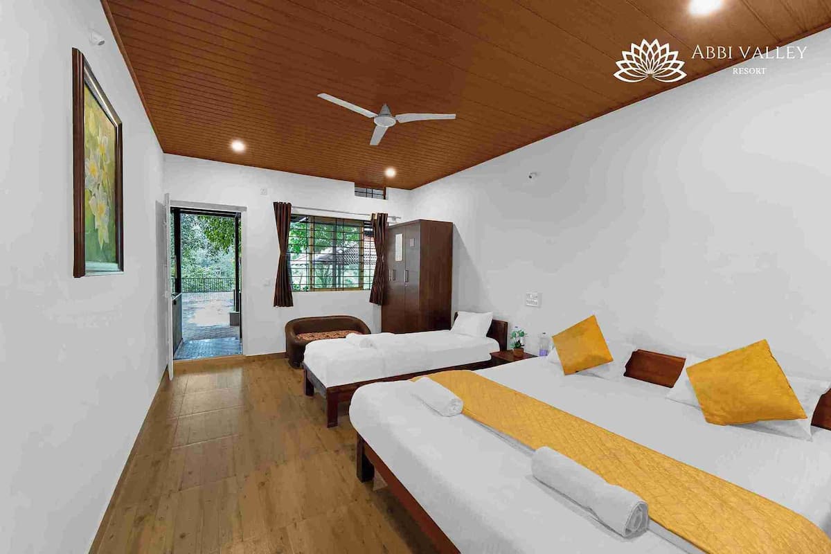 A hotel room with two beds, wooden flooring, a ceiling fan, and a view of the outdoors.