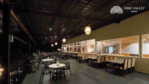 A spacious restaurant with high ceilings and modern lighting, featuring multiple dining areas with tables and chairs. - Abbi Valley Resorts  (Sakleshpur)