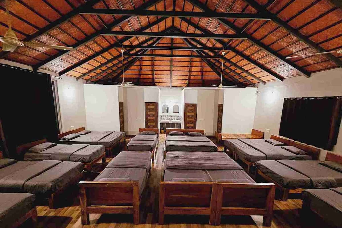 A room with multiple beds arranged in rows, a high wooden ceiling, and a central area with a white wall and a door.