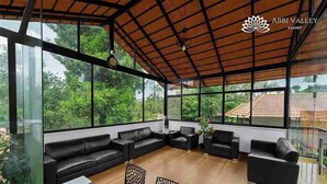 A spacious indoor area with a wooden ceiling, large windows, black leather sofas, and a table with chairs. - Abbi Valley Resorts  (Sakleshpur)