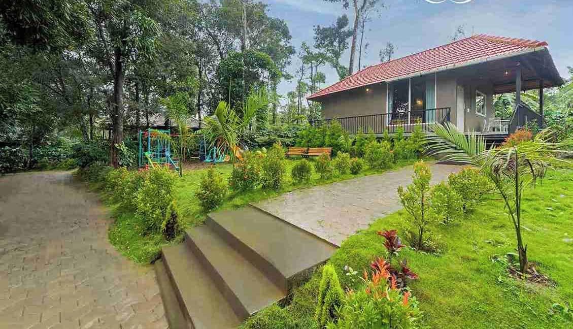 A resort with a red-roofed building, surrounded by lush greenery and a paved pathway leading to the entrance.