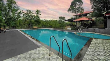 Una piscina con un borde de baldosas, una zona de estar techada y un pabellón.