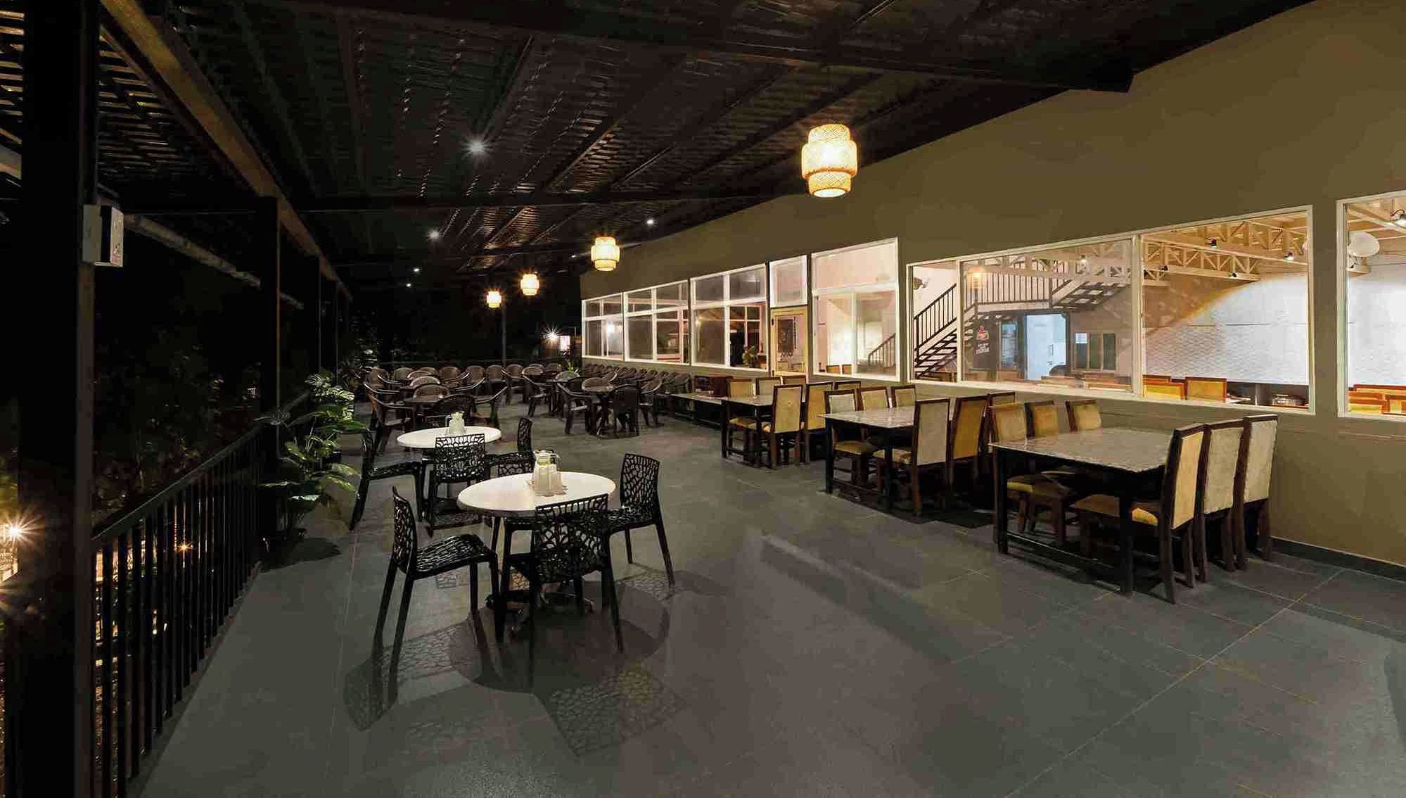 A spacious restaurant with high ceilings and modern lighting, featuring multiple dining areas with tables and chairs.