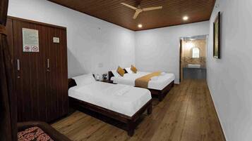 Habitación de hotel con dos camas, piso de madera, ventilador de techo y baño con lavamanos y espejo.