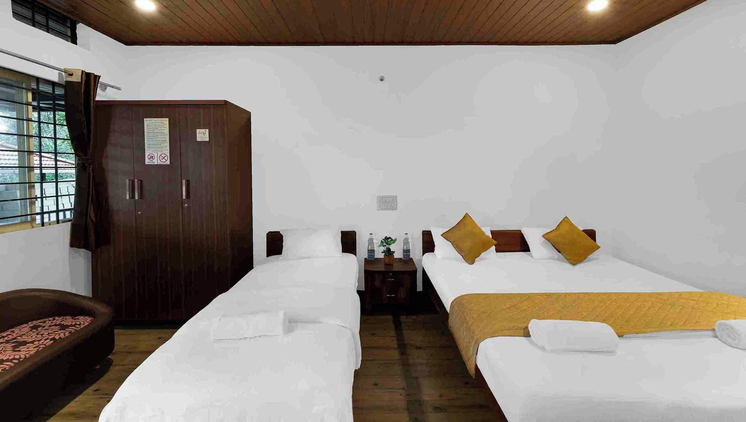 A hotel room with two beds, a wardrobe, a desk with a plant, and a ceiling fan.