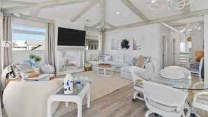 A spacious living room with a fireplace, white furniture, and a large TV. - Experience luxury at SeaSons at the Point, a stunning oceanfront rental in Oak Island. (Oak Island)