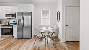A modern kitchen with white cabinets, stainless steel appliances, a round dining table with chairs, and a wooden floor. - New Breezy Cottage - King Bed - Mini-Golf - Park (Youngsville)