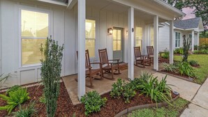 A house with a porch, white siding, and a garden with plants and mulch. - New Breezy Cottage - King Bed - Mini-Golf - Park (Youngsville)