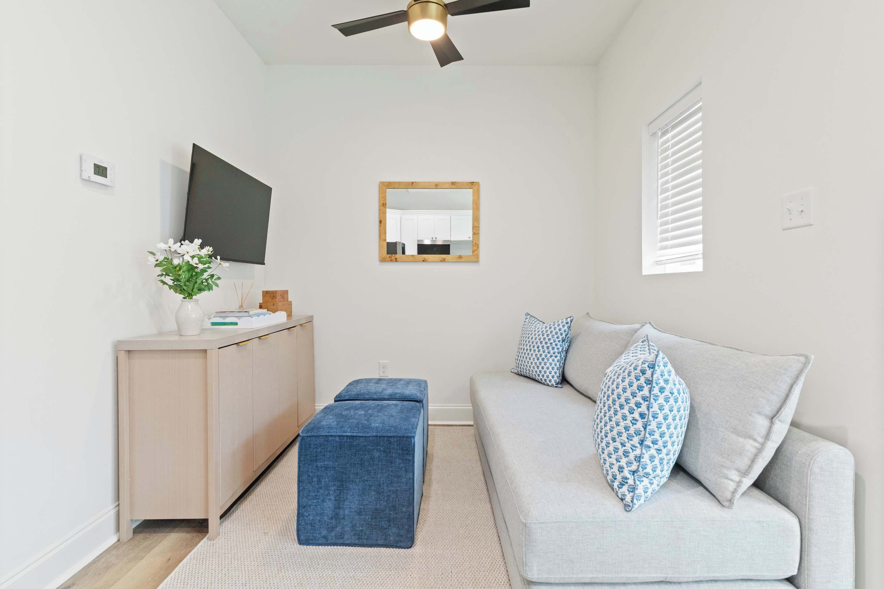 Un salon moderne comprenant un canapé, une table basse, un téléviseur, un ventilateur de plafond et une fenêtre avec des stores.