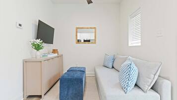Un salon moderne comprenant un canapé, une table basse, un téléviseur, un ventilateur de plafond et une fenêtre avec des stores.