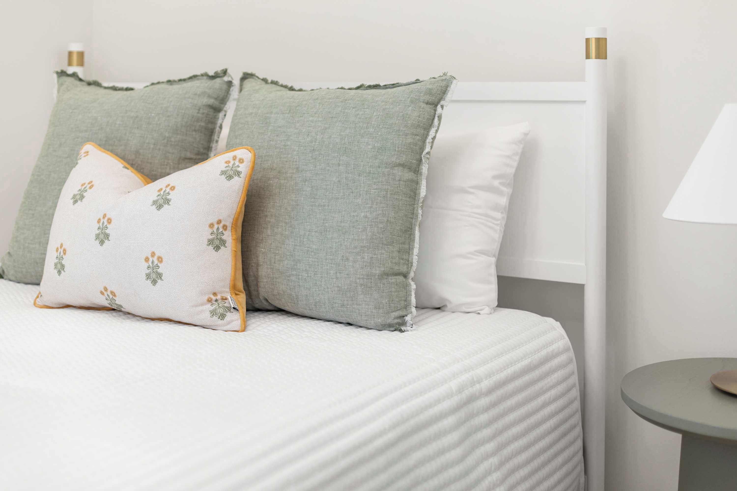 A bed with white bedding, two pillows, a small round table, and a lamp.