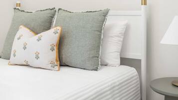 A bed with white bedding, two pillows, a small round table, and a lamp.