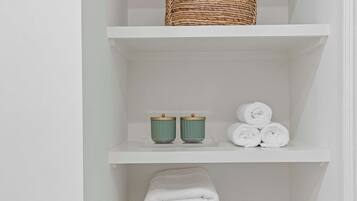 Een wit wandrek met een gevlochten mand, twee groene bekers en opgerolde handdoeken.