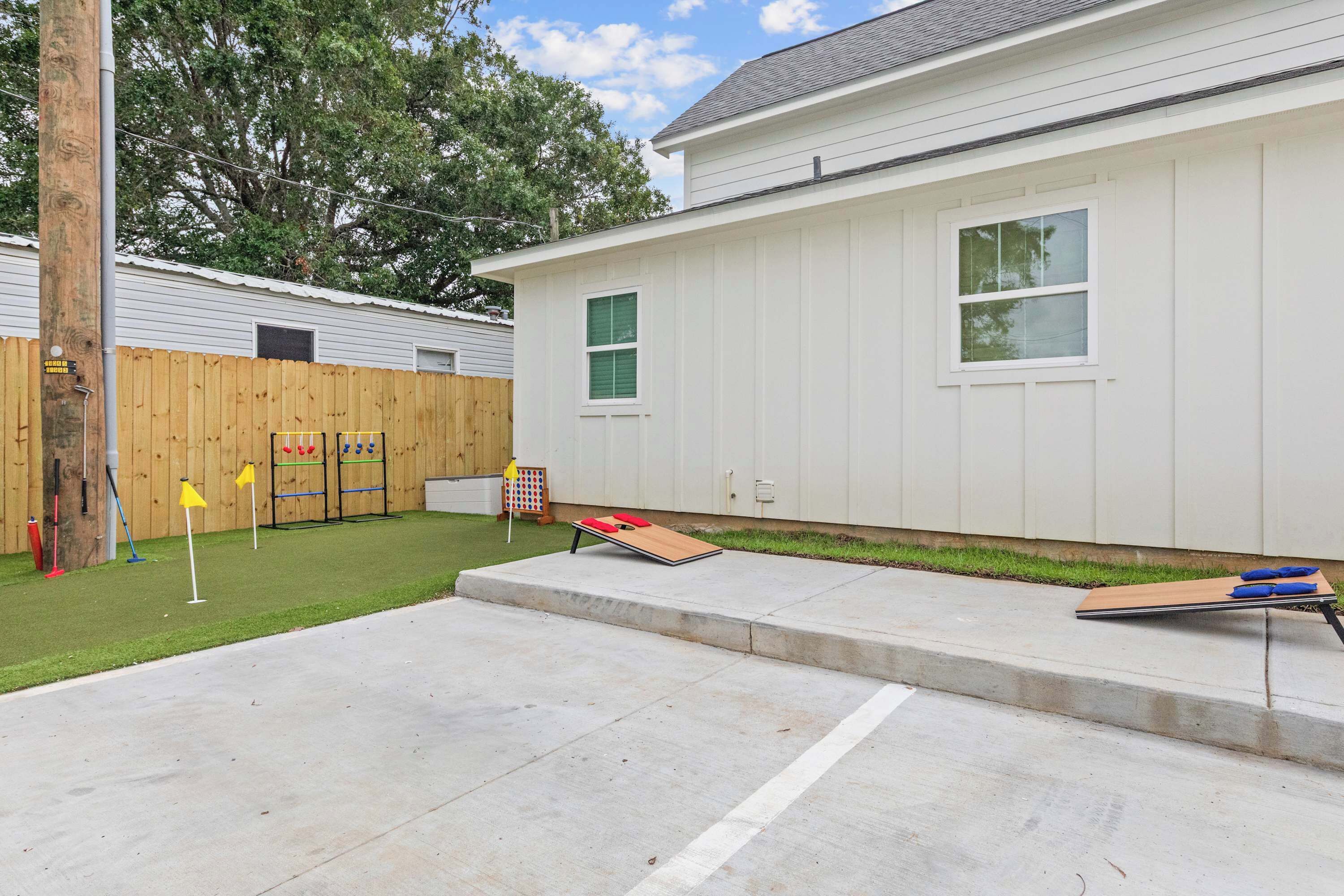 A residential backyard with a concrete patio, a wooden fence, and a small play area with a seesaw and yellow flags.