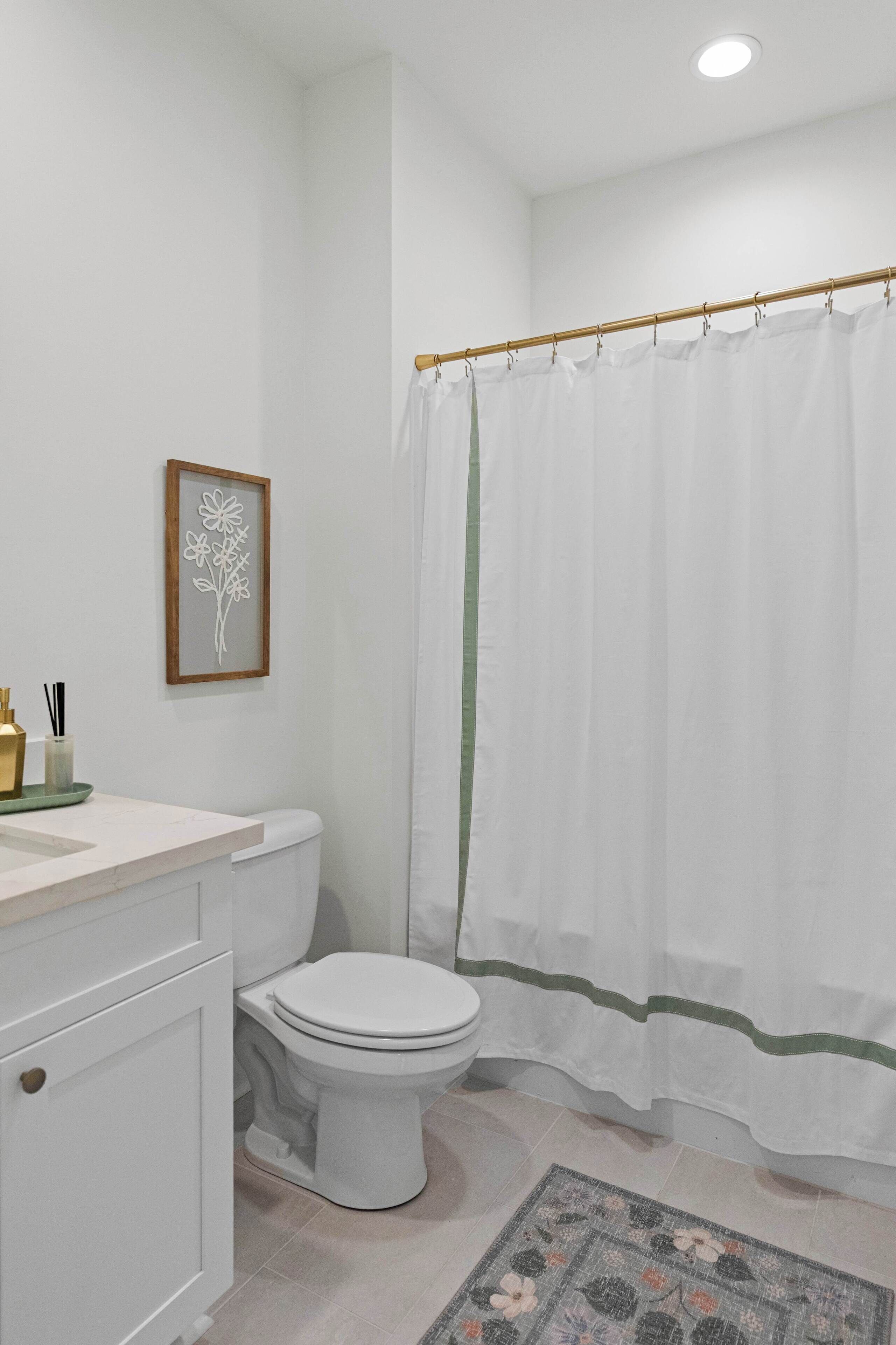 Un baño con inodoro, lavamanos con espejo, una obra de arte floral enmarco y cortina de ducha.