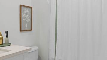 Un baño con inodoro, lavamanos con espejo, una obra de arte floral enmarco y cortina de ducha.